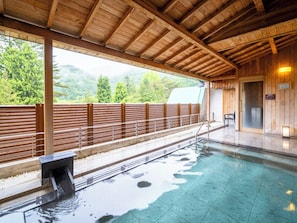 Piscina techada con techo de madera y vista a colinas verdes.