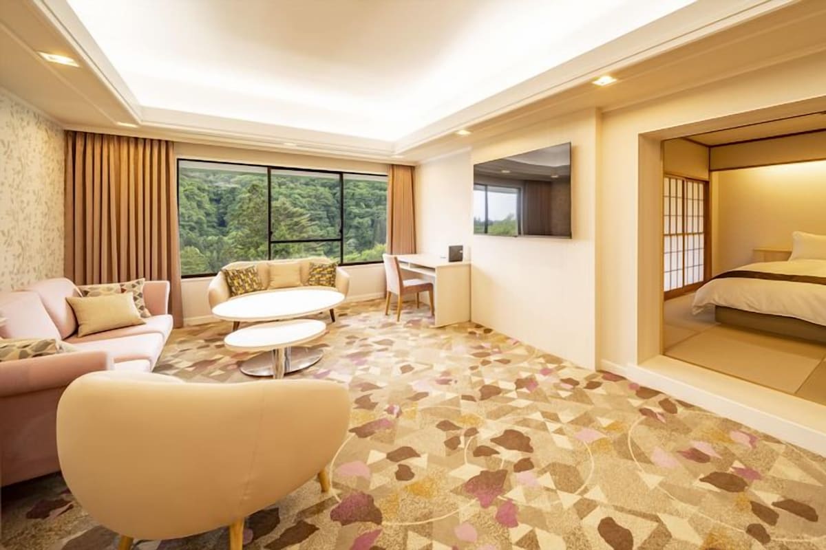 Ein Hotelzimmer mit einer Couch, einem Esstisch, einem Bett mit Blick und einem gemusterten Teppich.