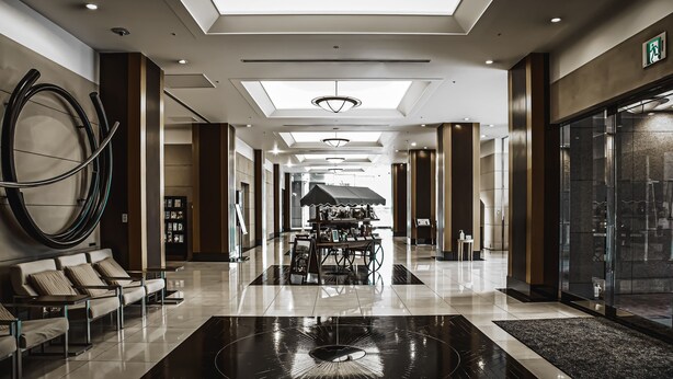 A modern hotel lobby with a central kiosk, seating area, and a large glass wall. - Oarks canal park hotel Toyama (Toyama)