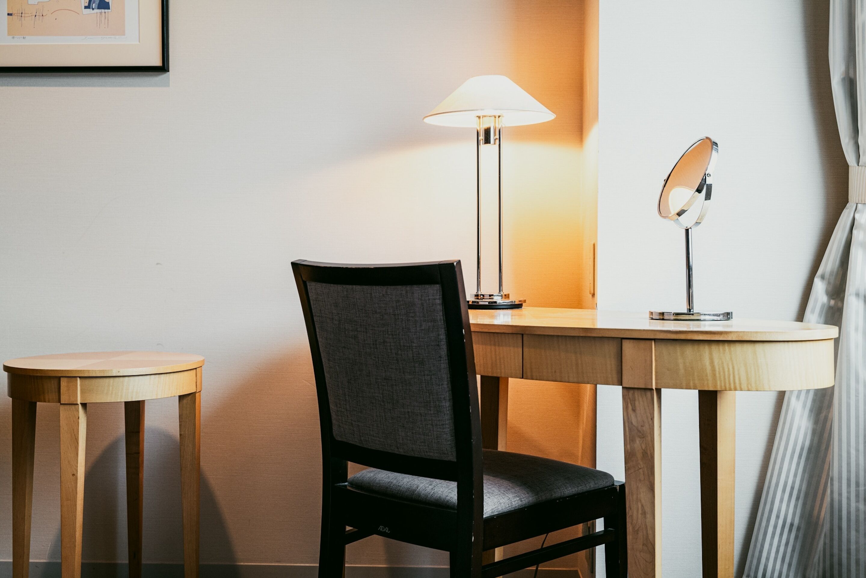 Una habitación con un escritorio de madera, una silla, una lámpara y un espejo.