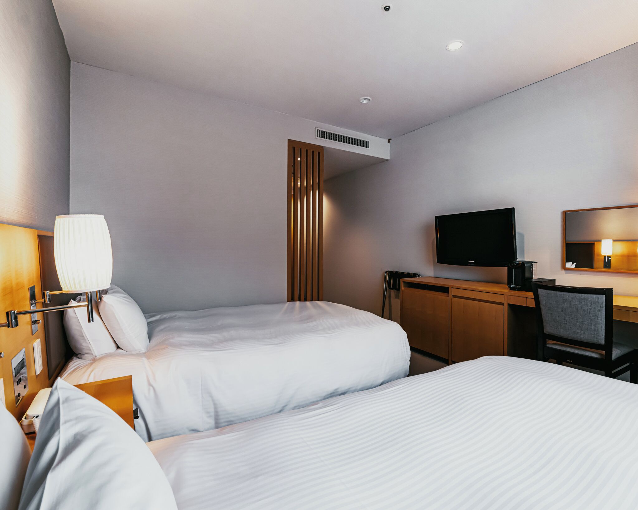 Ein Hotelzimmer mit zwei Betten, einem Schreibtisch, einem Fernseher und einem Spiegel.