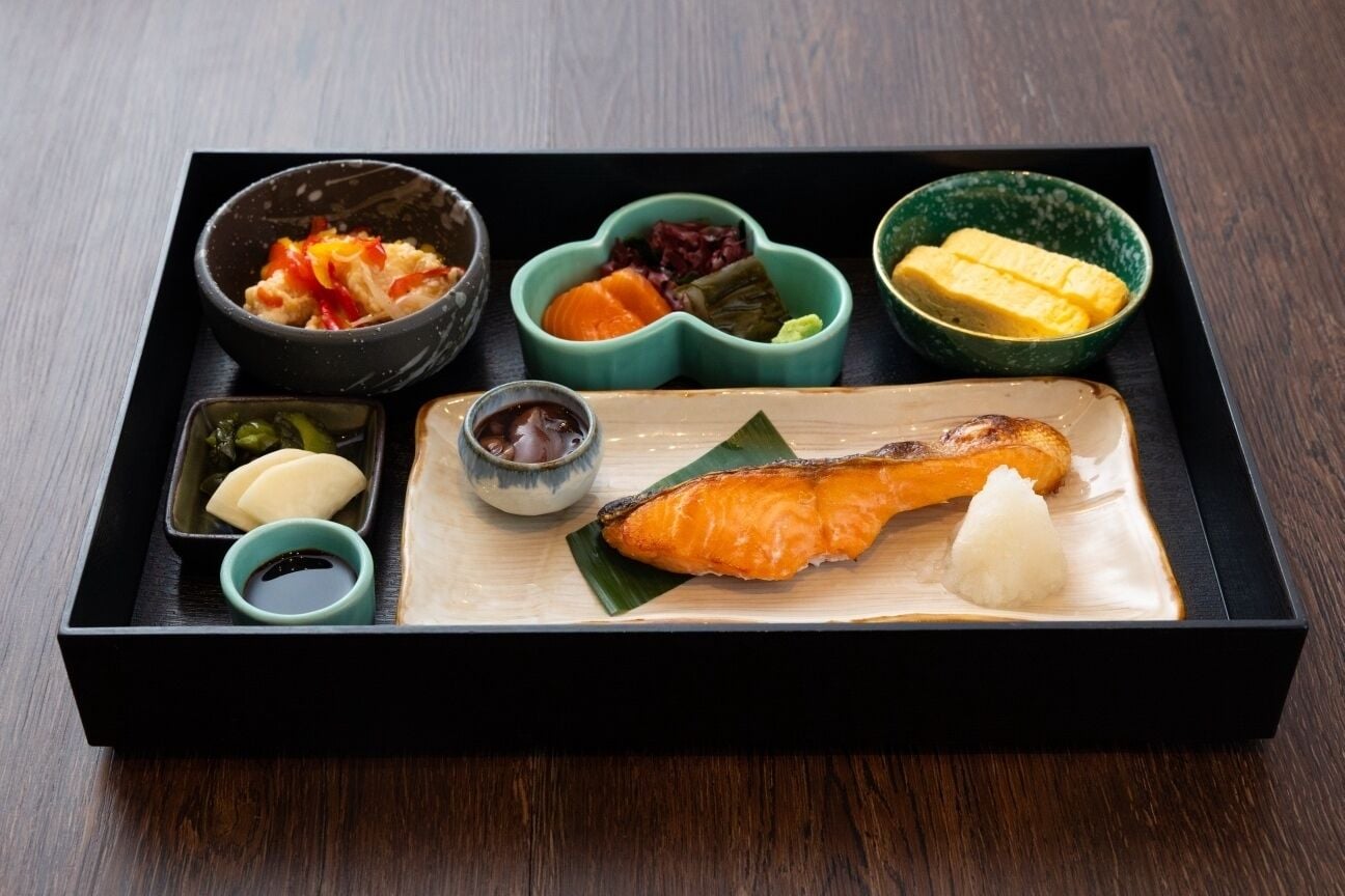 A traditional Japanese meal with salmon, rice, and various side dishes in a black tray.