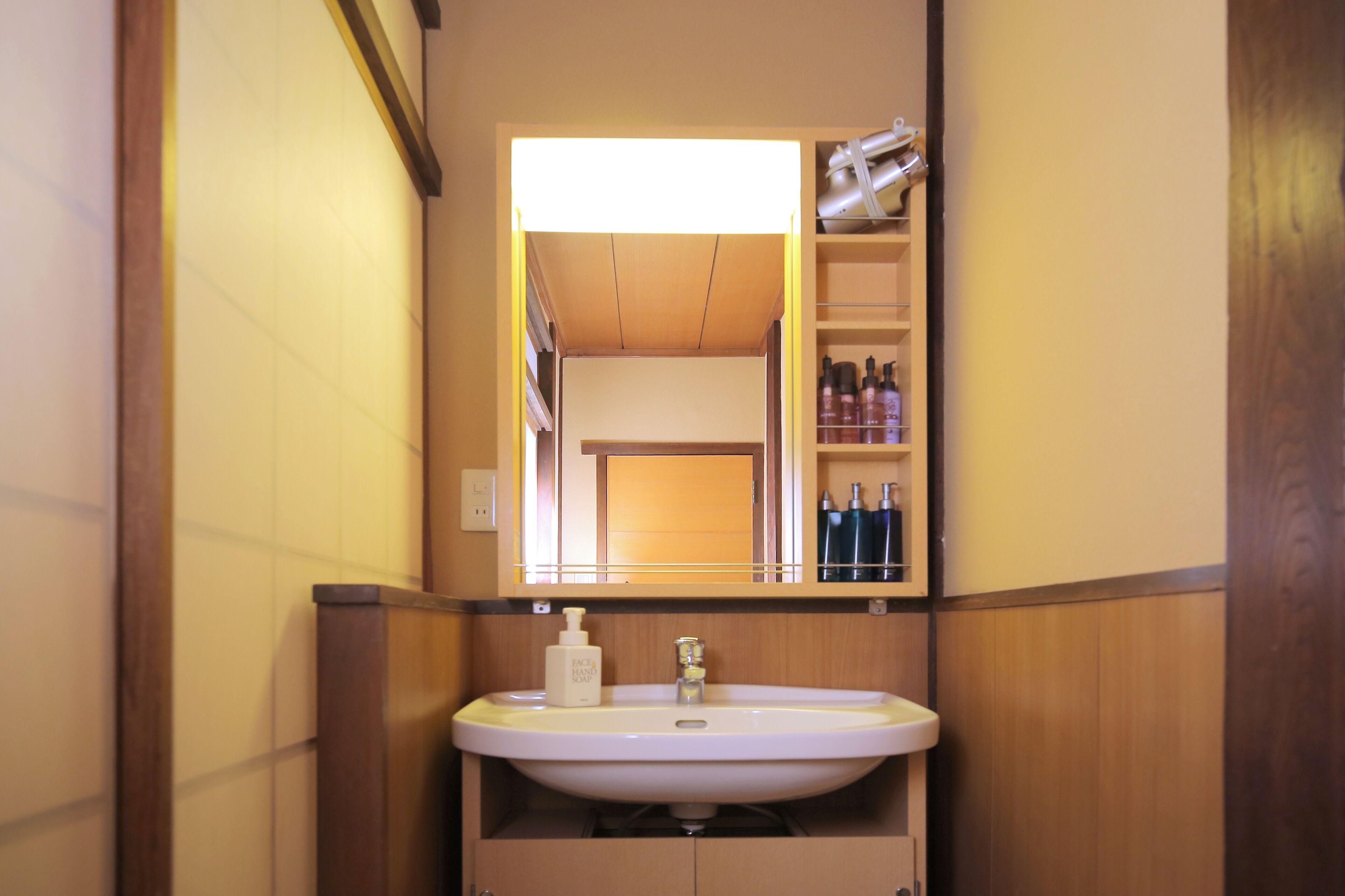 A bathroom with a white sink, a mirror above it, and a shelf with toiletries.