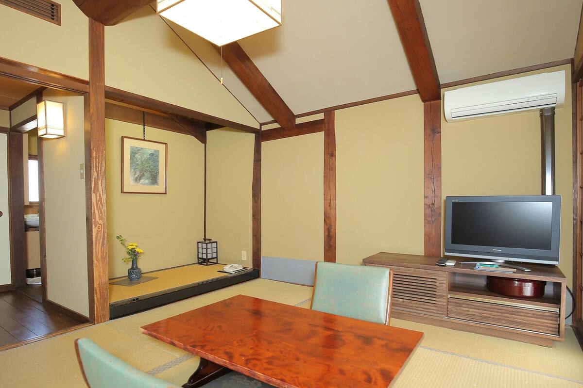 Une pièce de style japonais traditionnel, avec un sol recouvert de tatamis, une table basse et un téléviseur posé sur un meuble en bois.
