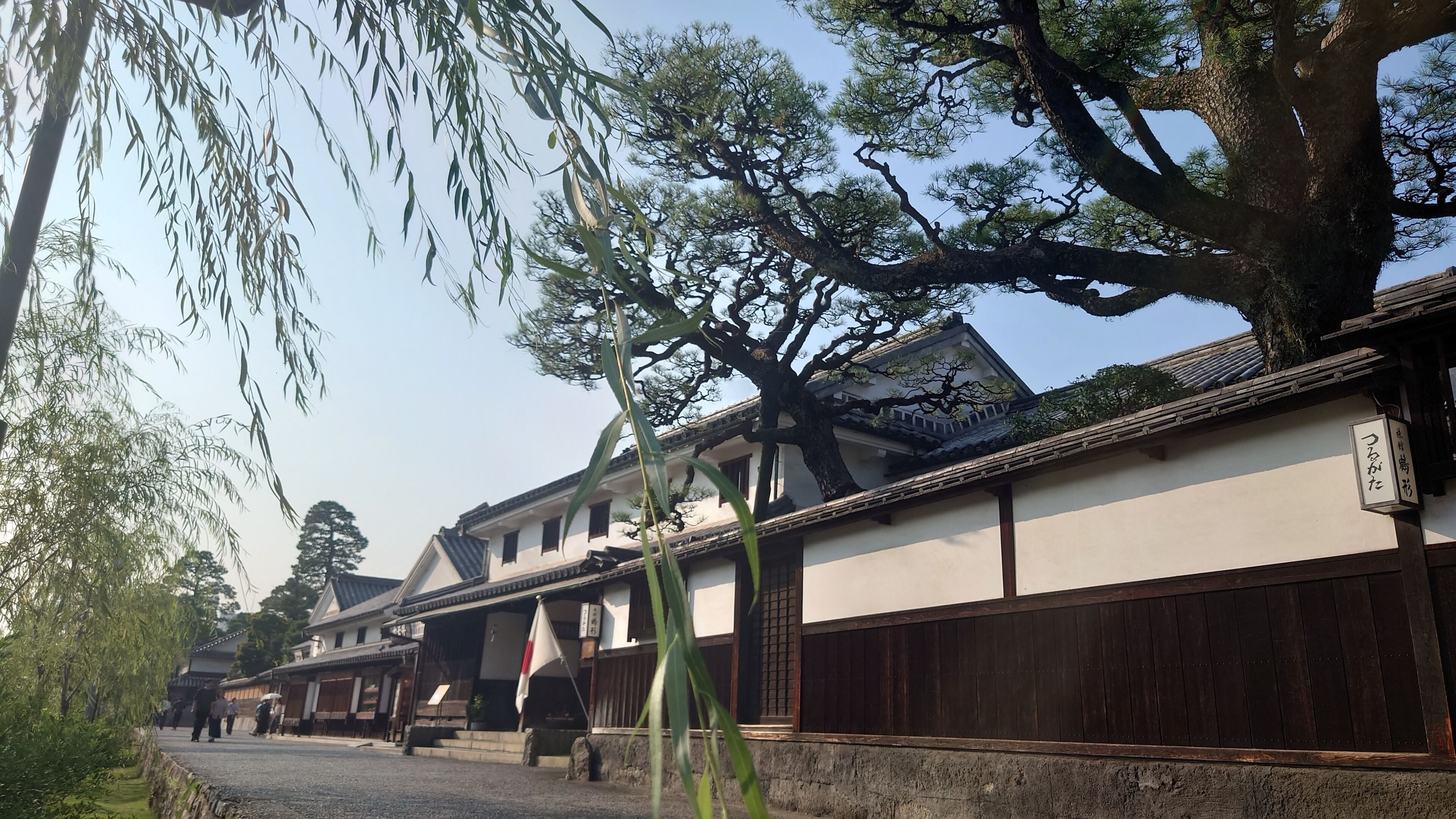 Um edifício japonês tradicional com cerca de madeira, uma bandeira e uma placa com caracteres japoneses.
