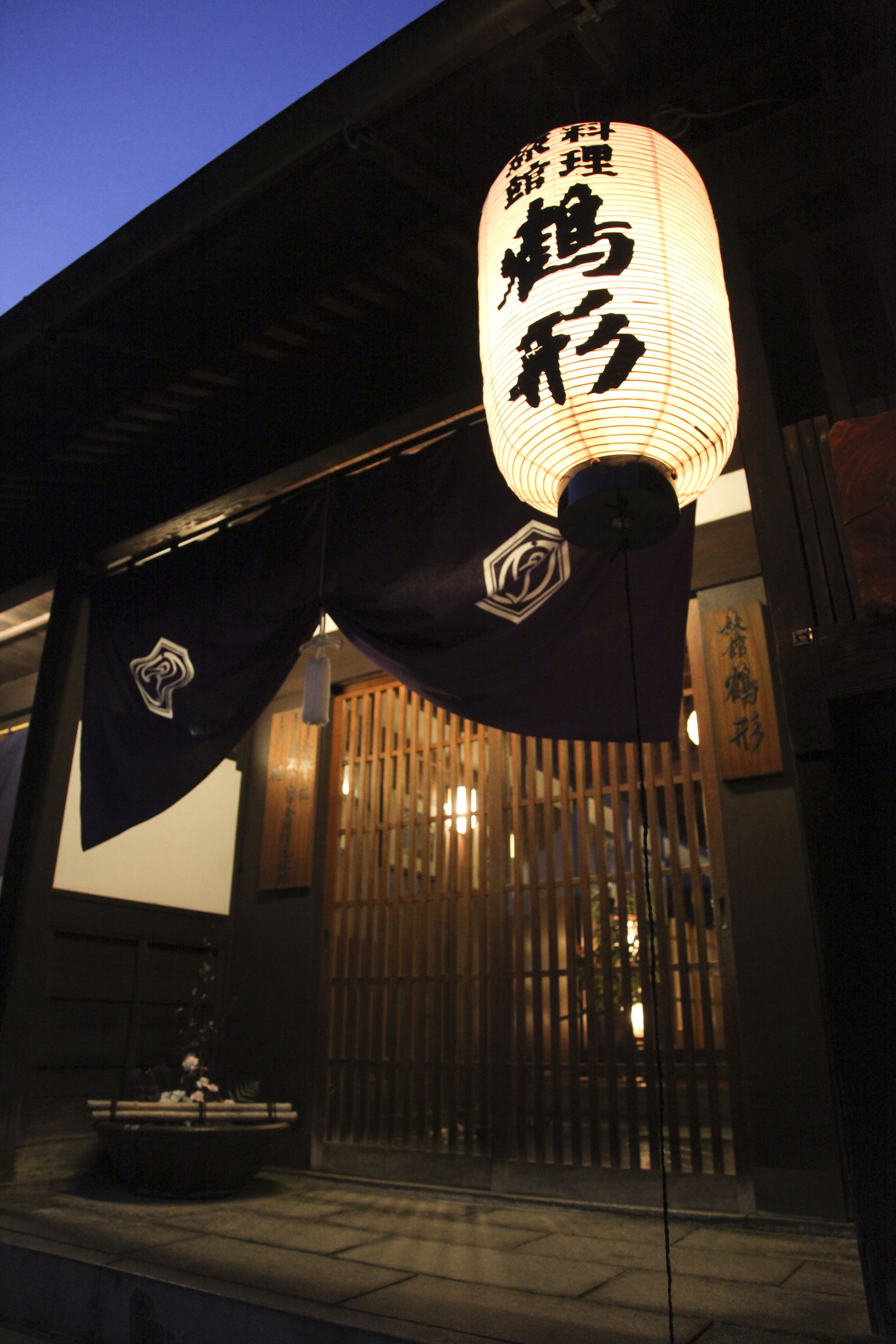 A traditional Japanese building with a lit lantern and a wooden gate.