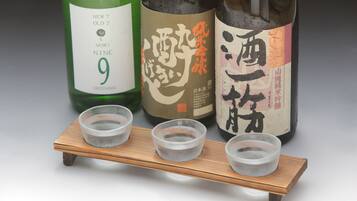 Three bottles of sake with labels, placed on a wooden stand with three small bowls in front.