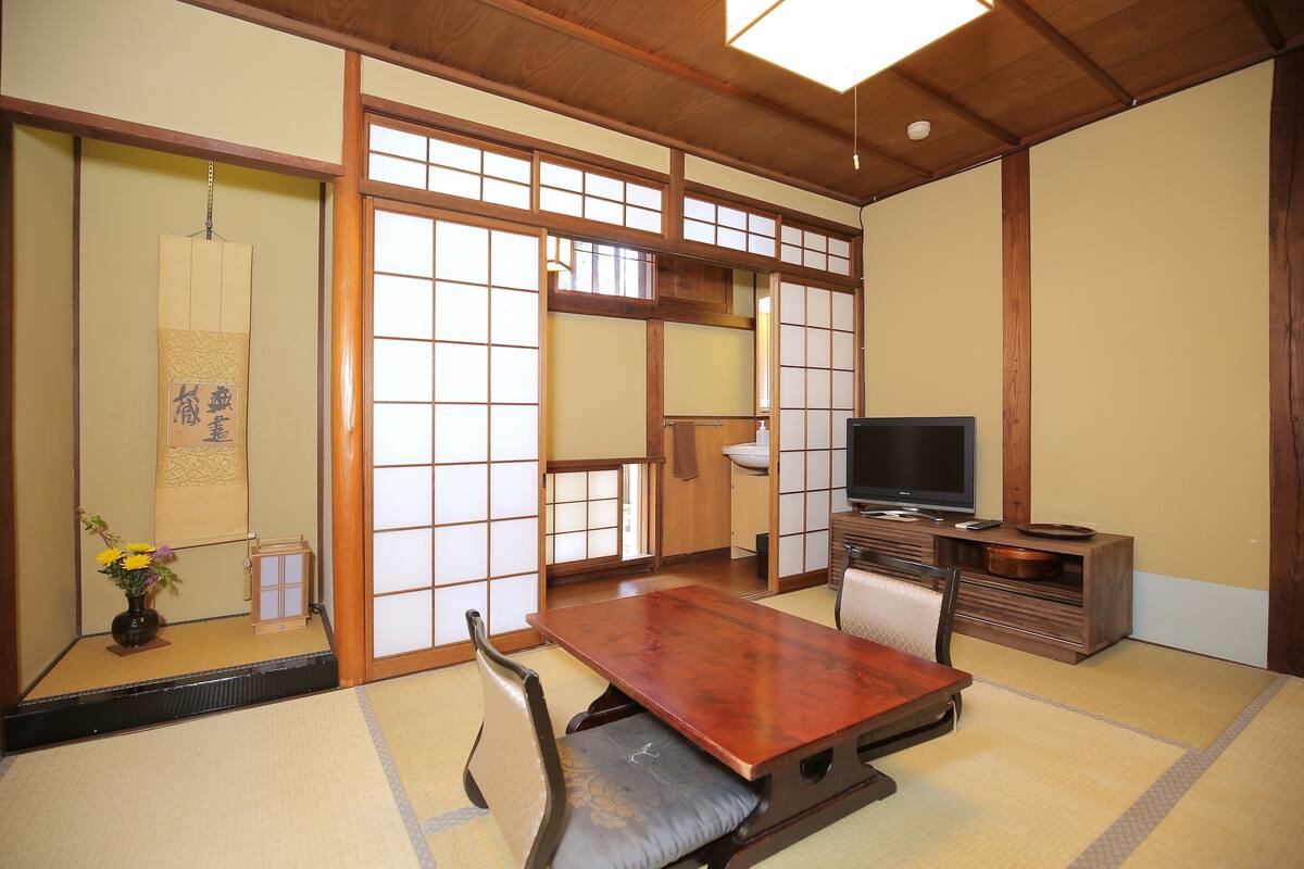 Une pièce de style japonais traditionnel, avec un sol recouvert de tatamis, une petite table en bois, un téléviseur et des portes coulissantes en papier de riz (shoji).