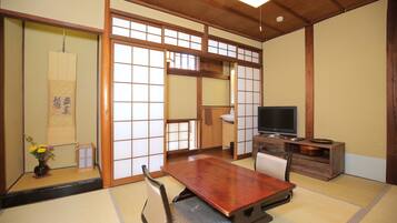 A traditional Japanese room with tatami flooring, a low wooden table, a television, and sliding shoji doors.