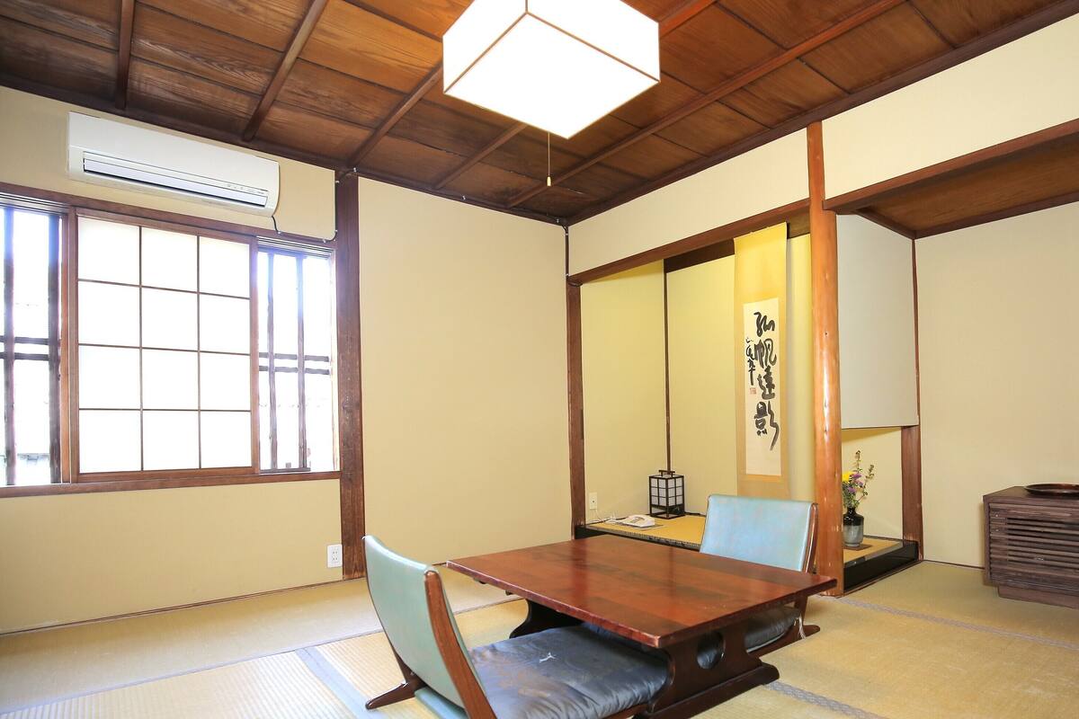 Une pièce de style japonais traditionnel, avec un sol recouvert de tatamis, une petite table en bois, une chaise, un téléviseur et une porte coulissante.