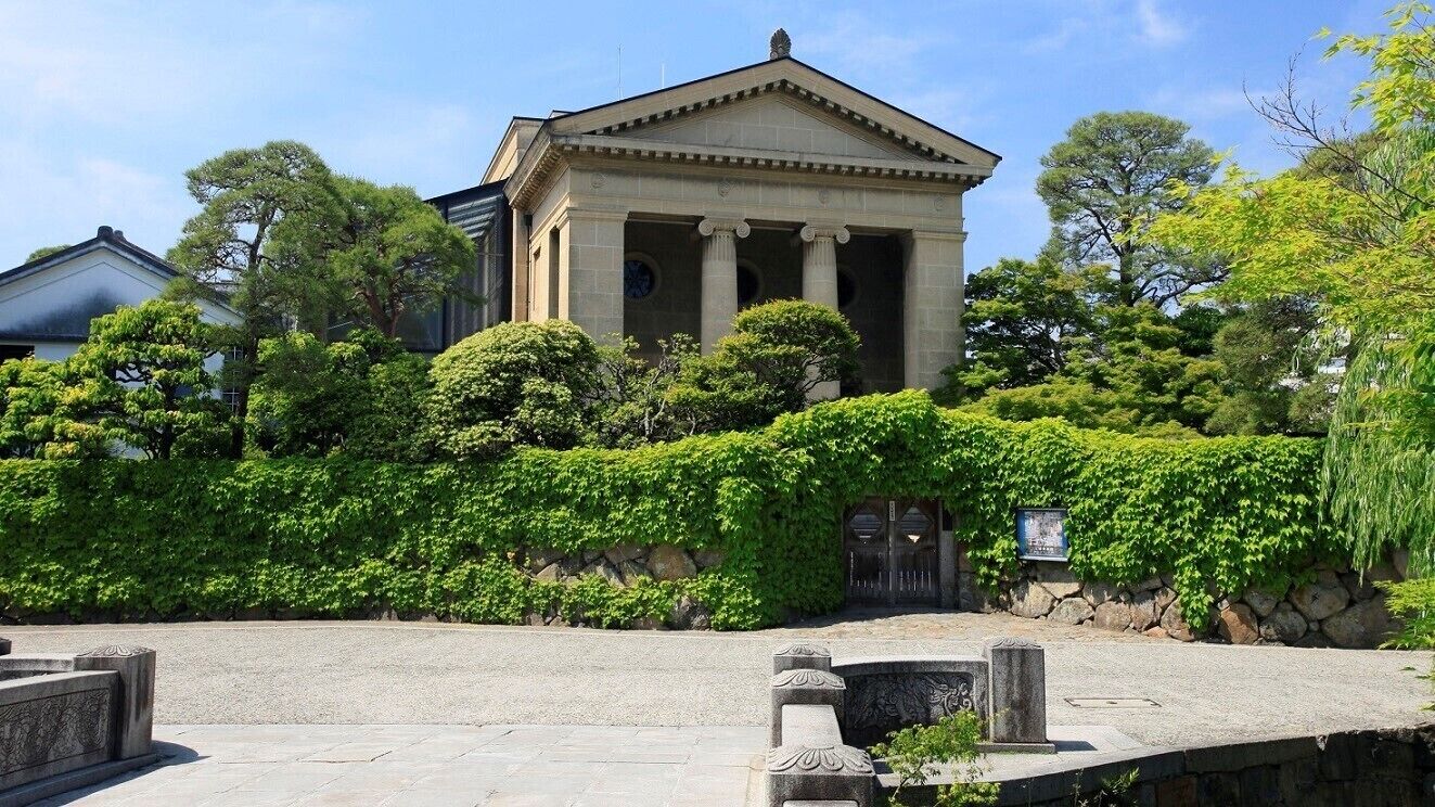 A classical building with columns, surrounded by lush greenery and a stone wall.