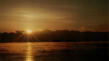 Ein Sonnenuntergang über einem Gewässer, im Hintergrund Berge.