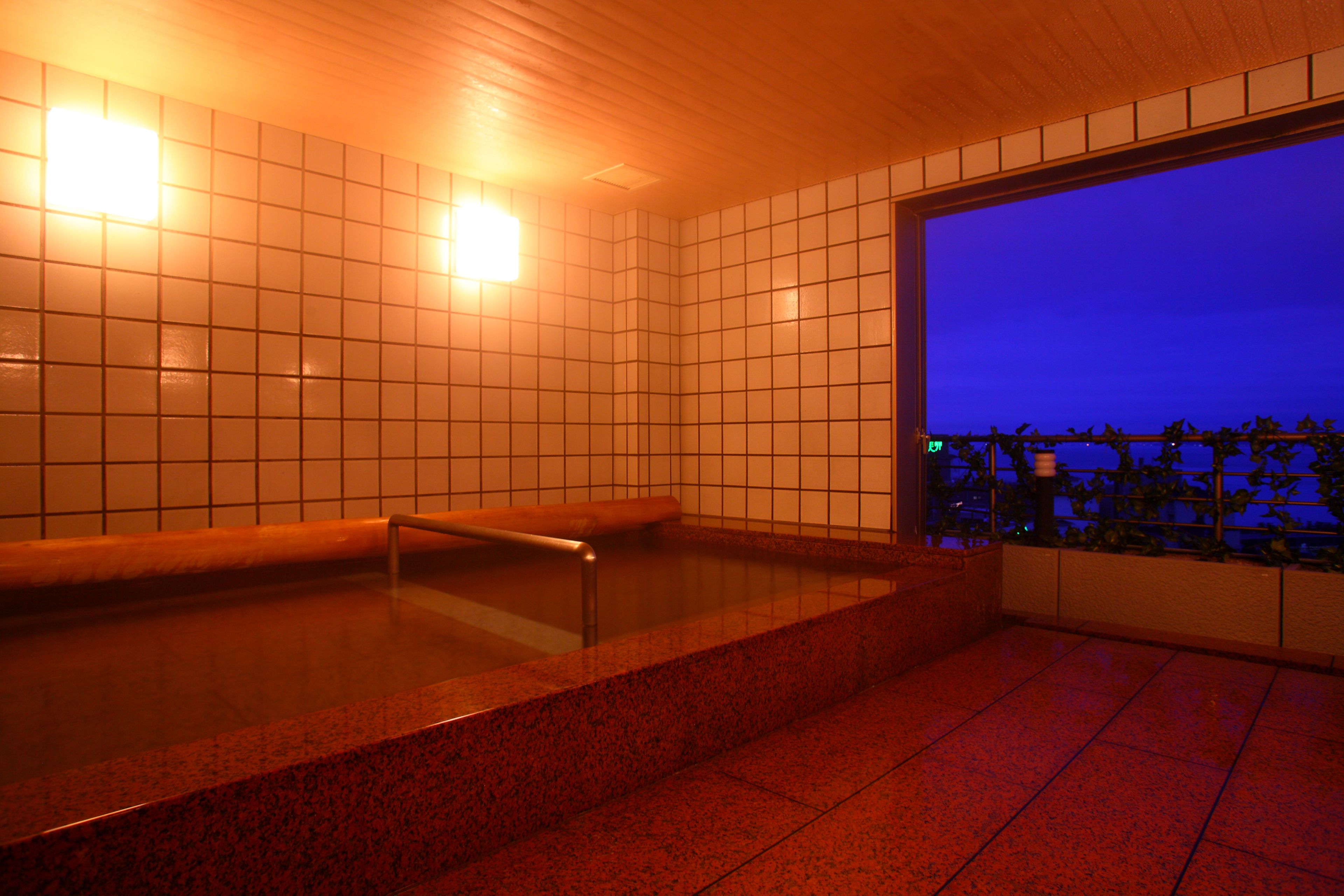 A spa area with a large hot tub, tiled walls, and a view of the city at dusk.