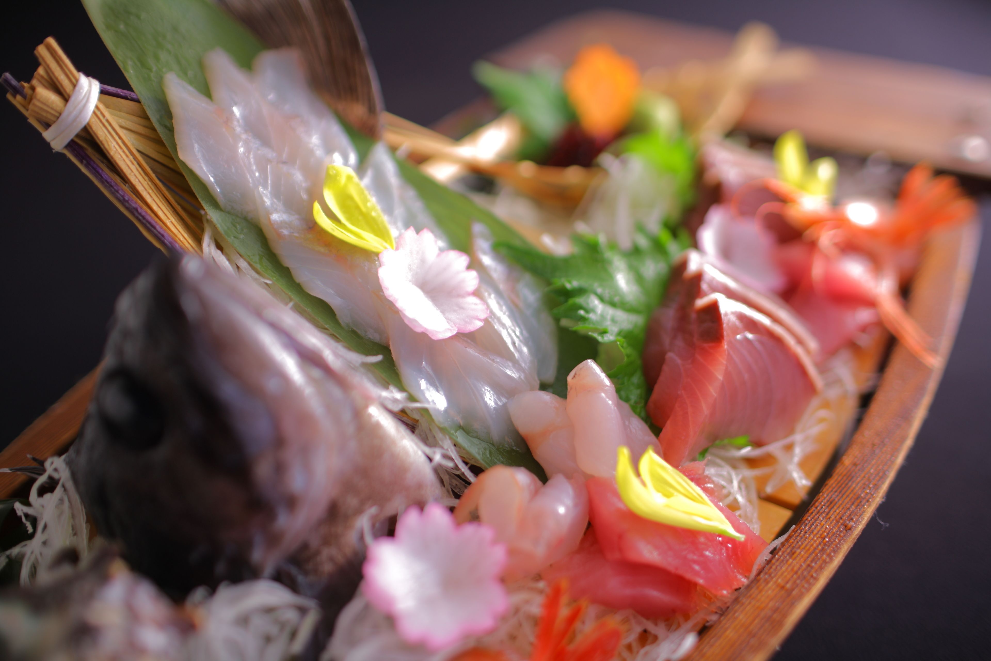 A wooden tray with various types of sushi, including fish and vegetables, arranged on a bed of shredded seaweed.