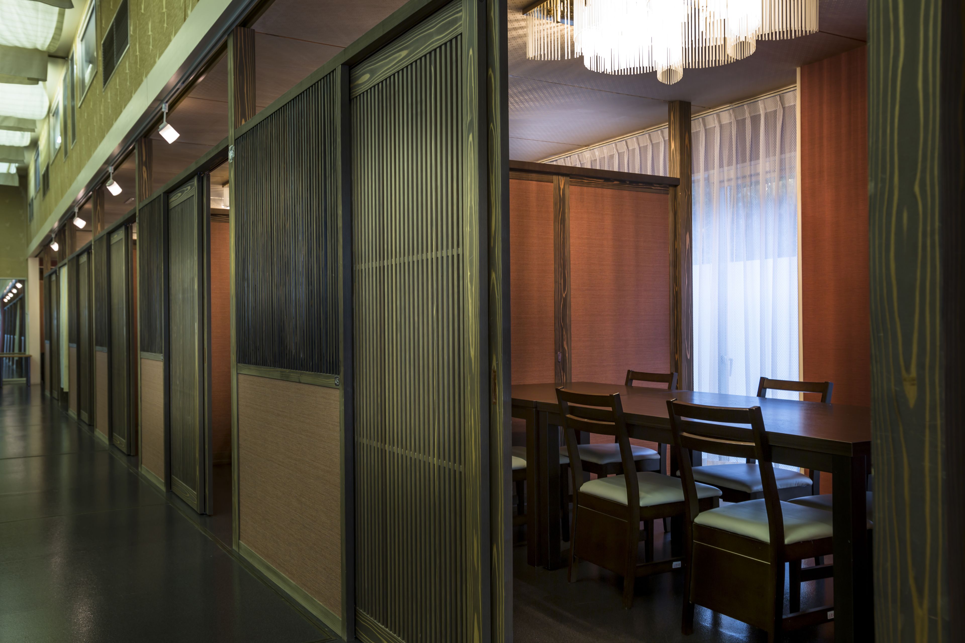 A corridor with sliding doors, a dining area with wooden tables and chairs, and a chandelier.