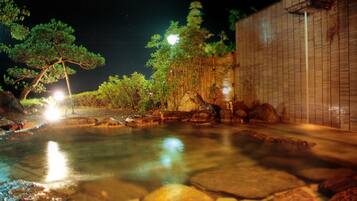 A nighttime view of a tranquil outdoor pool area with stone tiles, surrounded by trees and a bamboo fence.