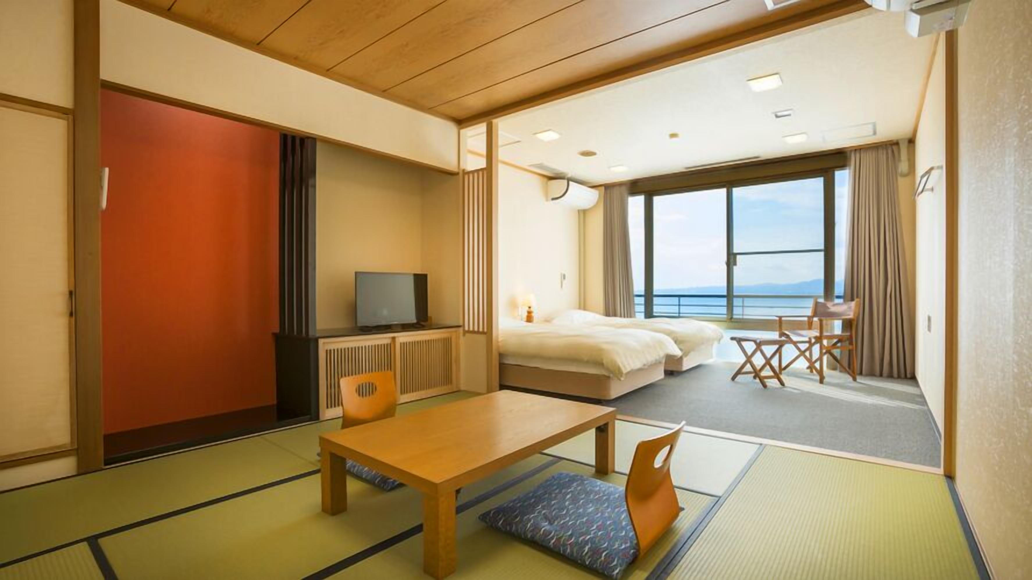 A hotel room with tatami flooring, a bed, a television, a desk, and a view of the sea.