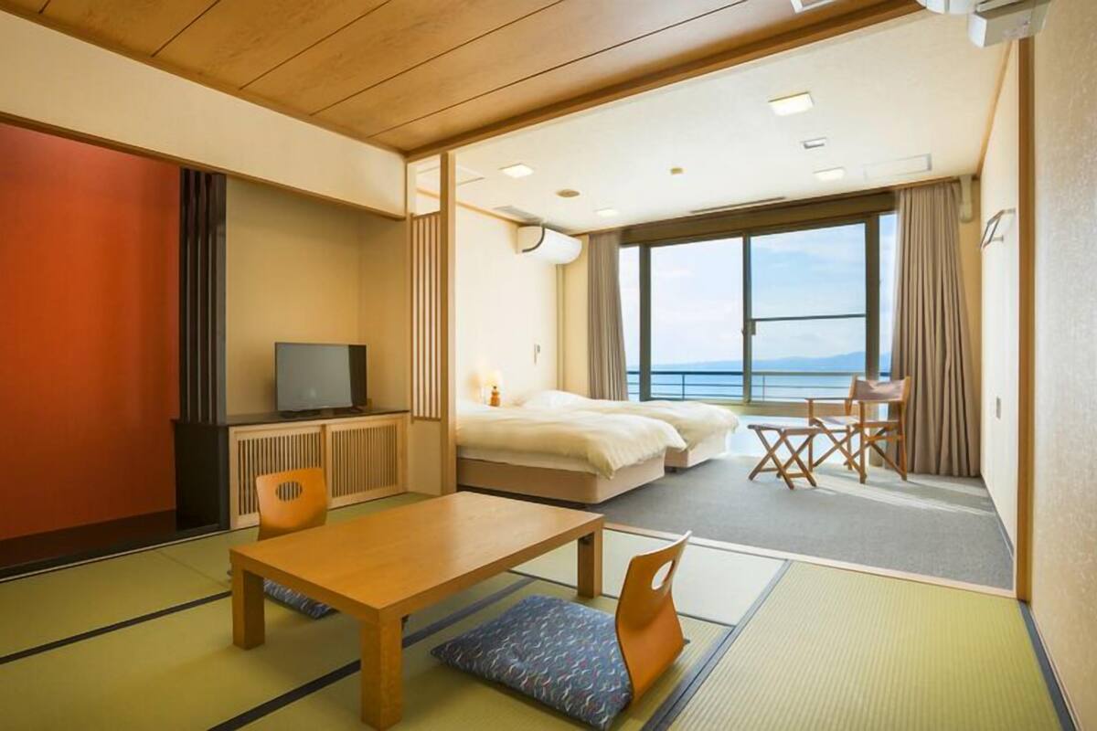 Ein Hotelzimmer mit Tatami-Böden, einem Bett, einem Fernseher, einem Schreibtisch und Meerblick.