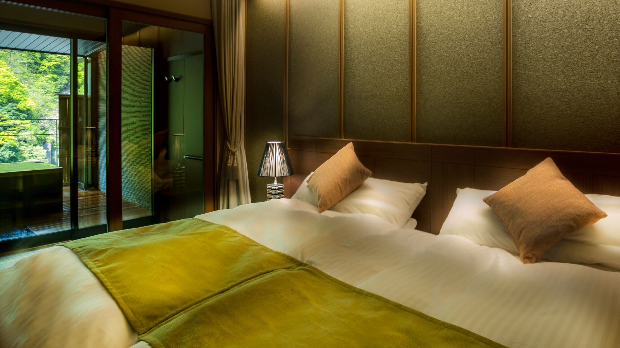 A hotel room with a bed, a nightstand, a lamp, and a view of a balcony.