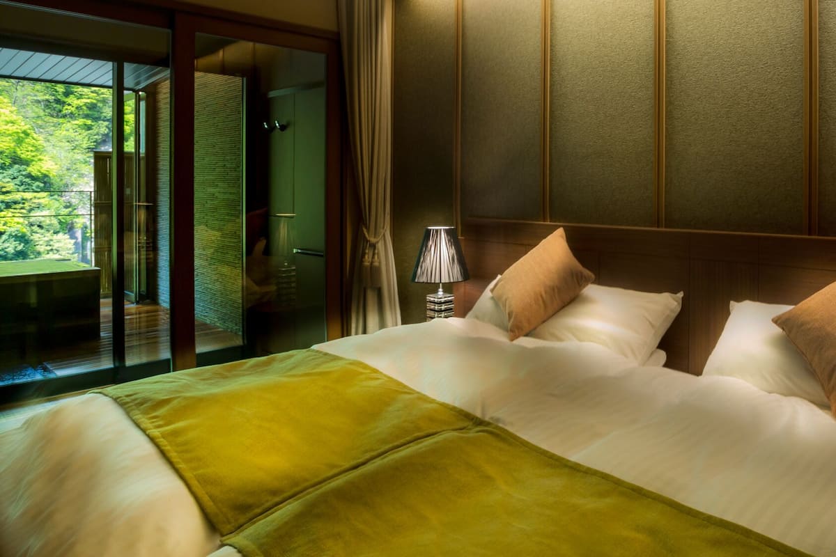 A hotel room with a bed, a nightstand, a lamp, and a view of a balcony.