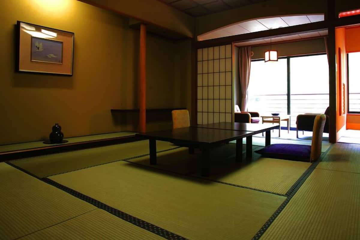 A tatami mat room with a low table and chairs, a framed picture on the wall, and a sliding door leading to a balcony.