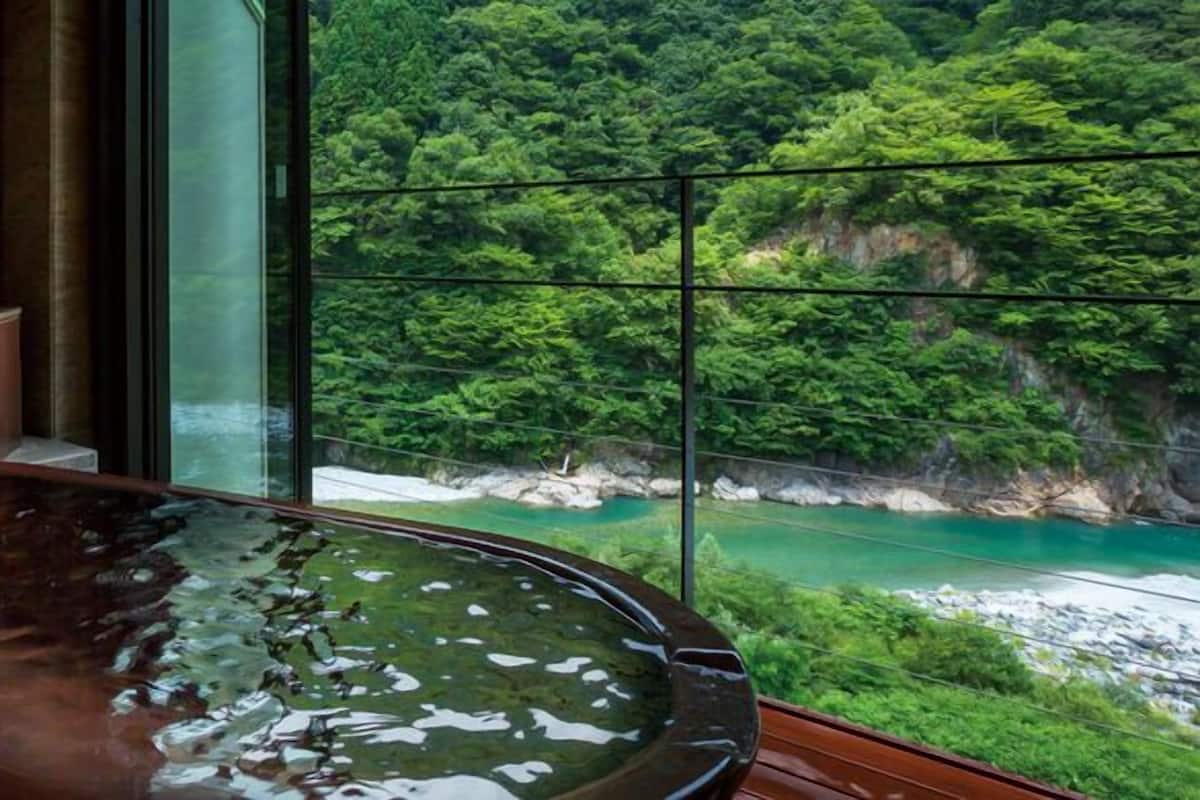 A hot tub with a view of a forested cliff and a turquoise river.