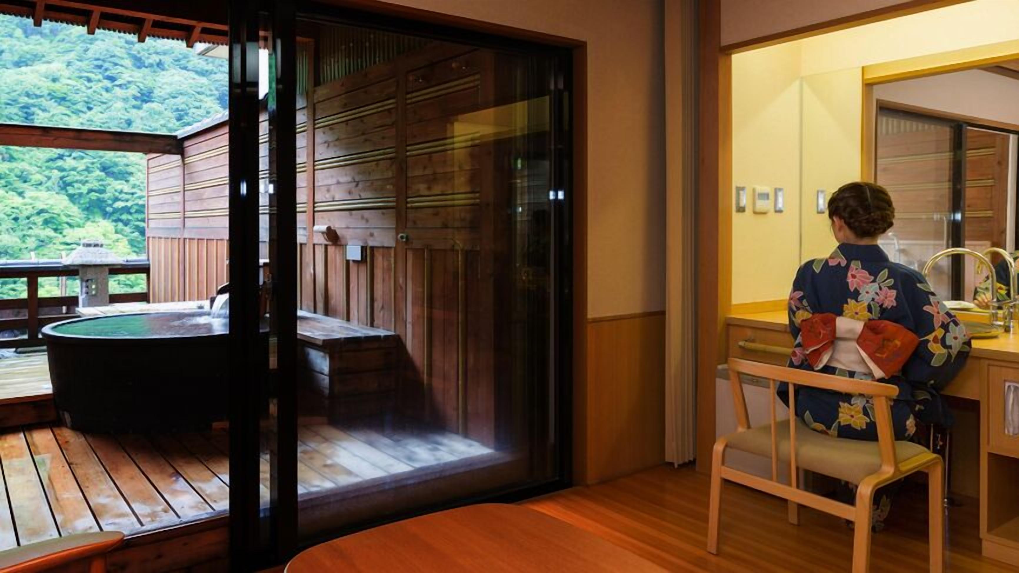 Una terrassa de fusta amb un banyera d'hidromassatge, una porta corredissa de vidre que dona a una habitació amb un lavabo i una cadira.