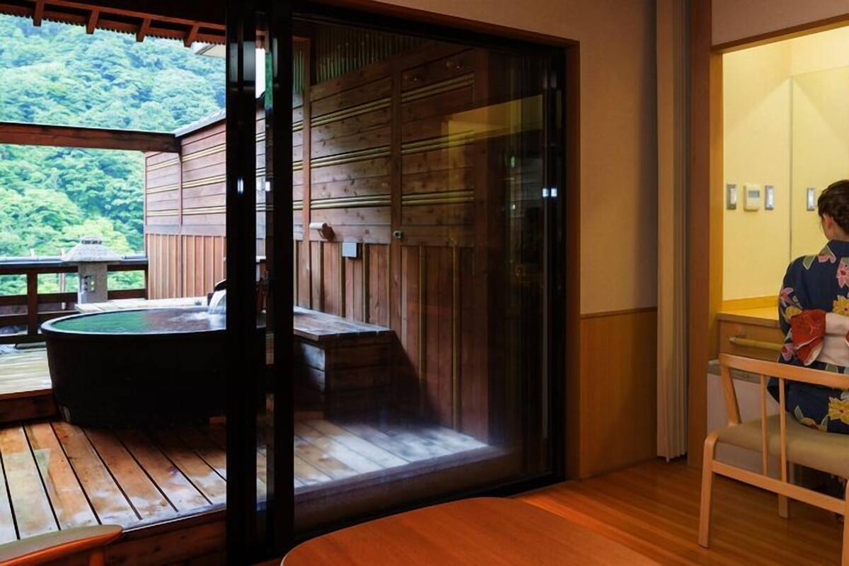 A wooden deck with a hot tub, a sliding glass door leading to a room with a sink and a chair.