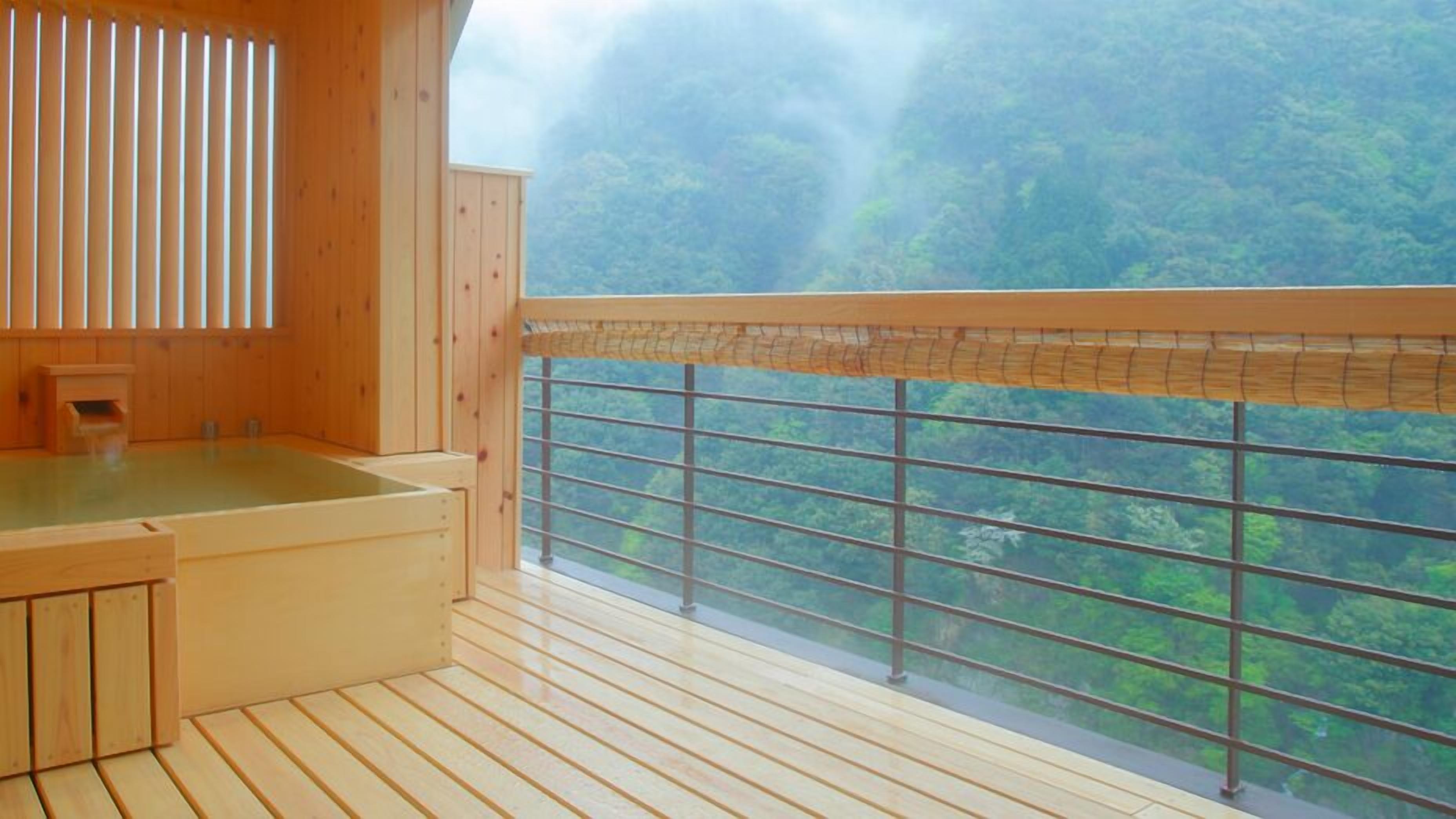 A wooden room with a wooden bathtub, a window with a view of a forest, and a bamboo blind.