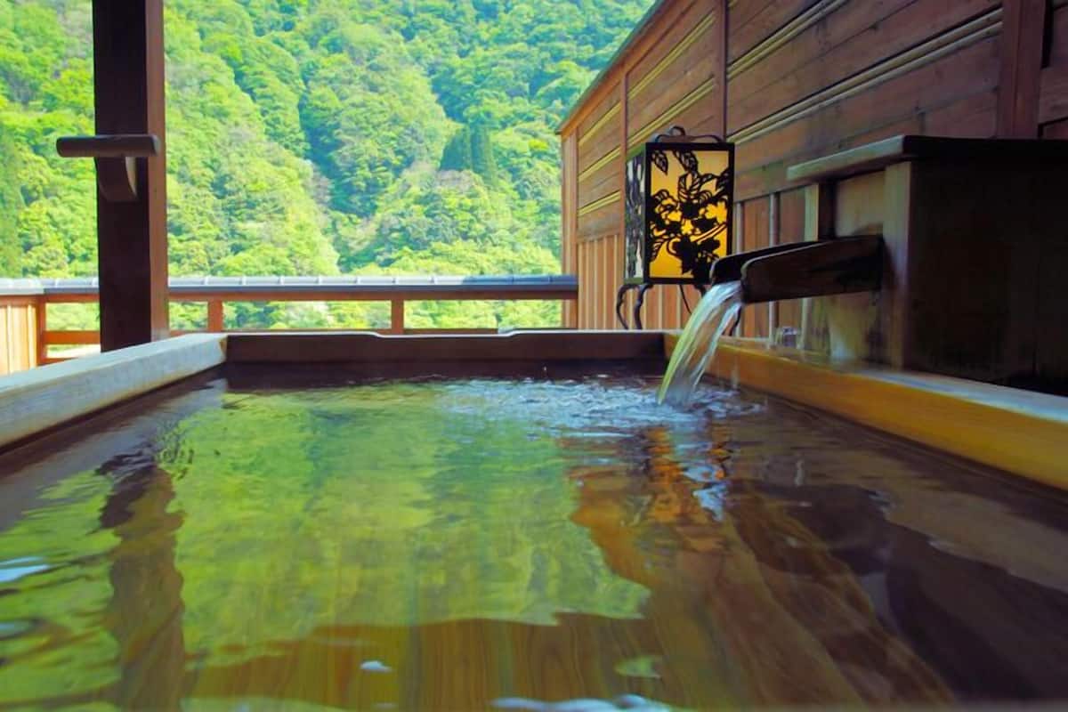 A hot spring bath with a wooden deck and a view of a forested mountain.