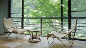 Una habitación con ventanas amplias, dos sillones de mimbre y una pequeña mesa redonda.