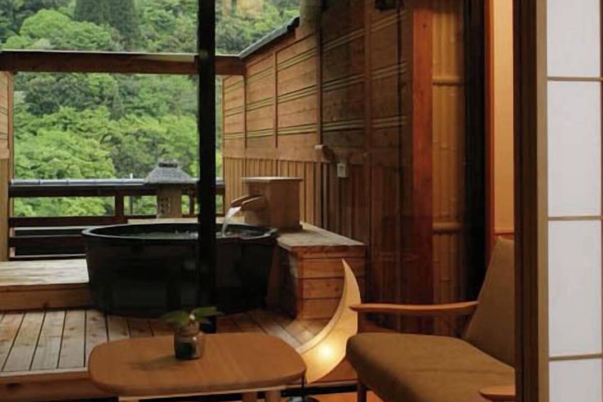 A room with a wooden interior, a hot tub, a table with a plant, and a view of greenery outside.