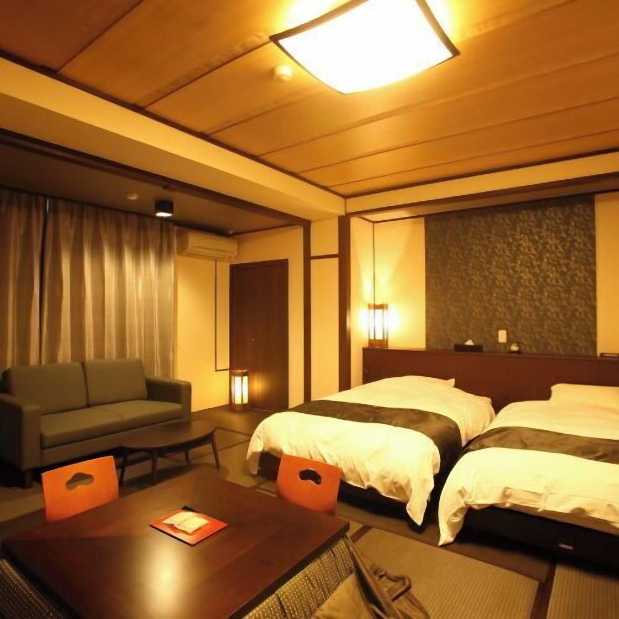 A hotel room with a sofa, two beds, a table, and a lamp.