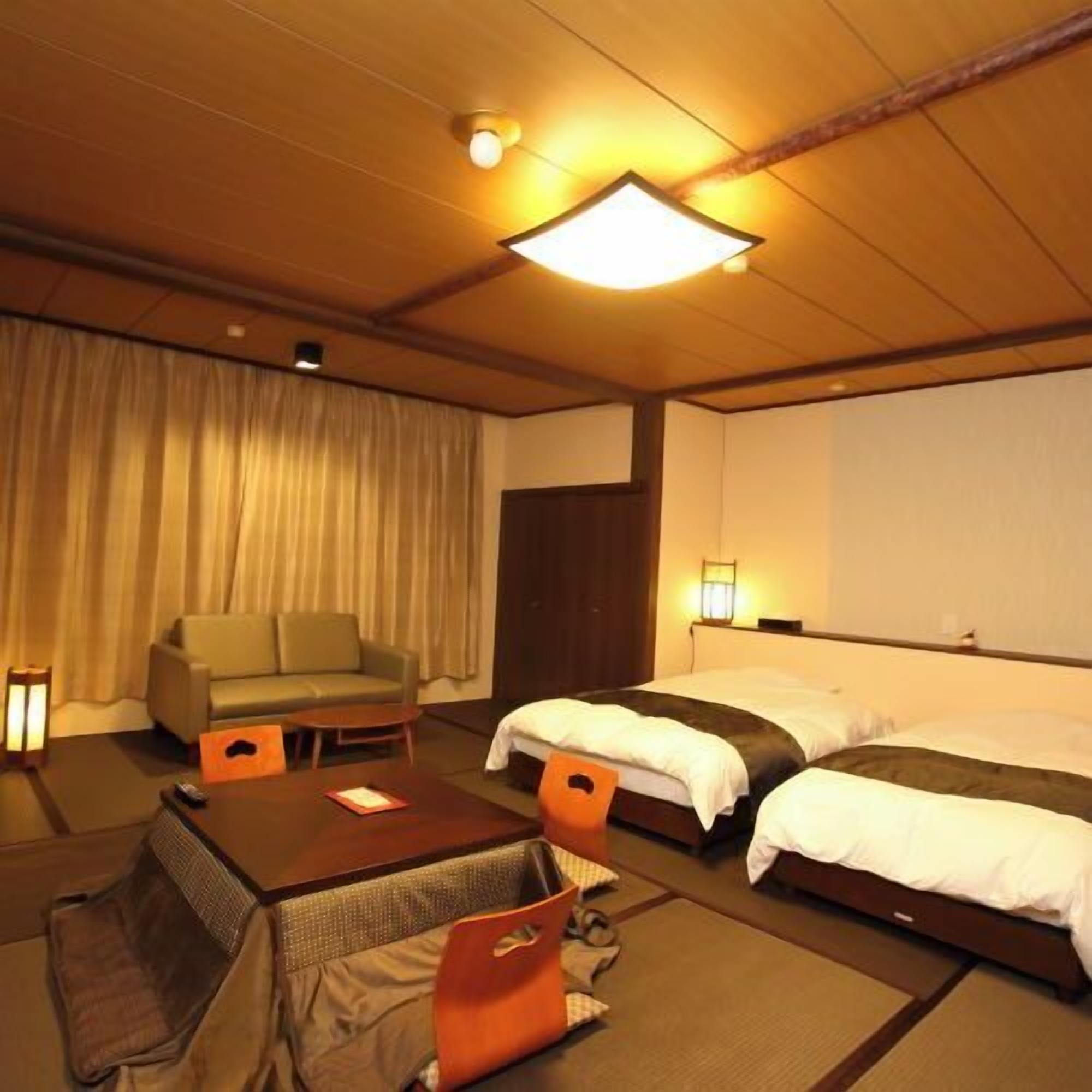 A hotel room with a sofa, two beds, a small table, and a curtain.