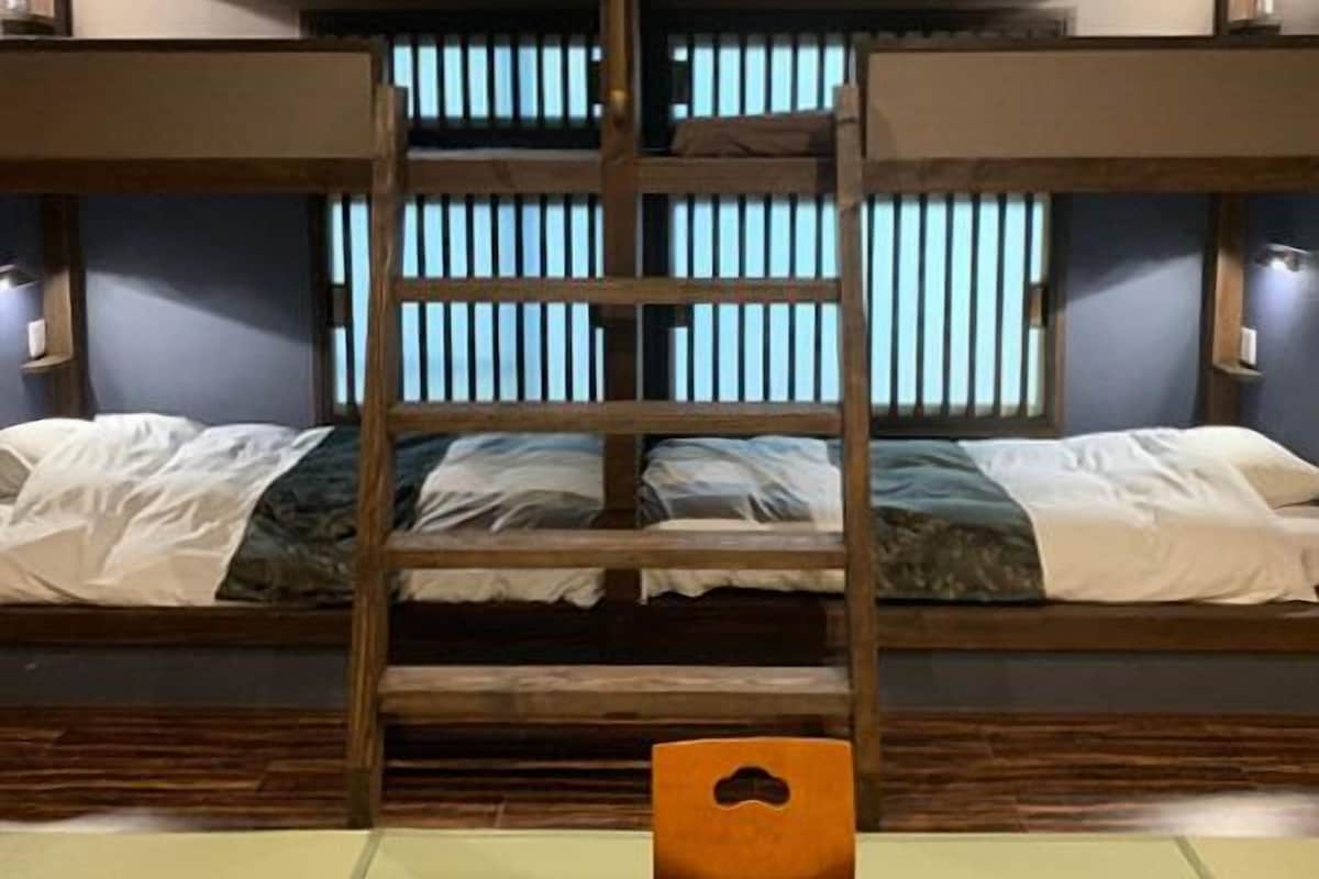 A bunk bed room with a ladder, wooden headboard, and a window with vertical blinds.