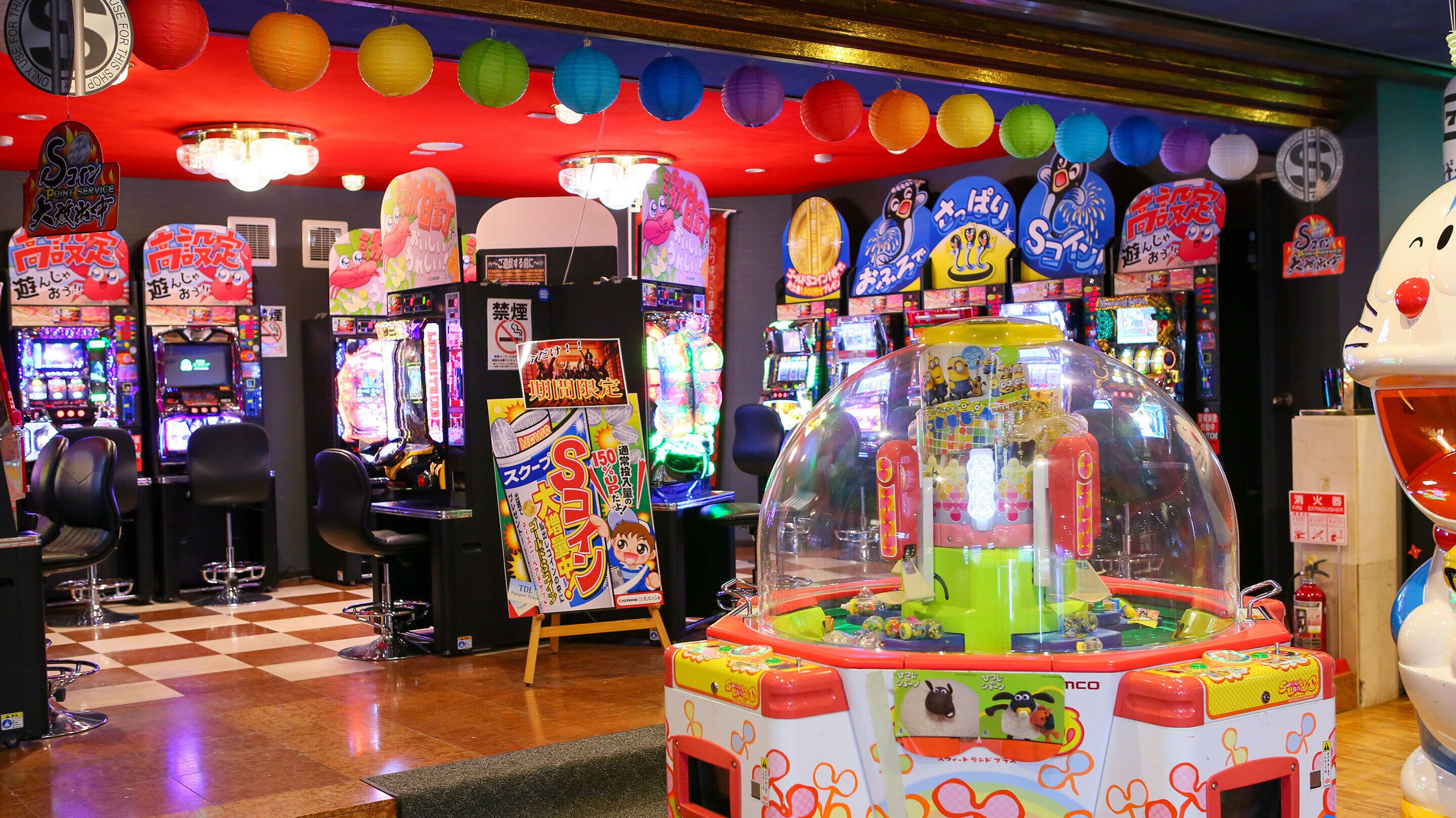 A brightly lit arcade with various gaming machines, including a prominent Minion-themed claw machine.
