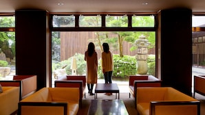 A room with a view of a garden, featuring a stone lantern and wooden fence. There are yellow chairs and a small table. - Ooedo Onsen Monogatari Awara (Awara)