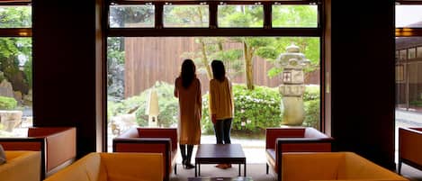 A room with a view of a garden, featuring a stone lantern and wooden fence. There are yellow chairs and a small table.