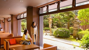 A hotel lobby with seating areas and a view of a garden with stone lanterns and greenery. - Ooedo Onsen Monogatari Awara (Awara)