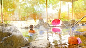A hot spring area with rocks, a wooden structure, and a pink umbrella. - Ooedo Onsen Monogatari Awara (Awara)