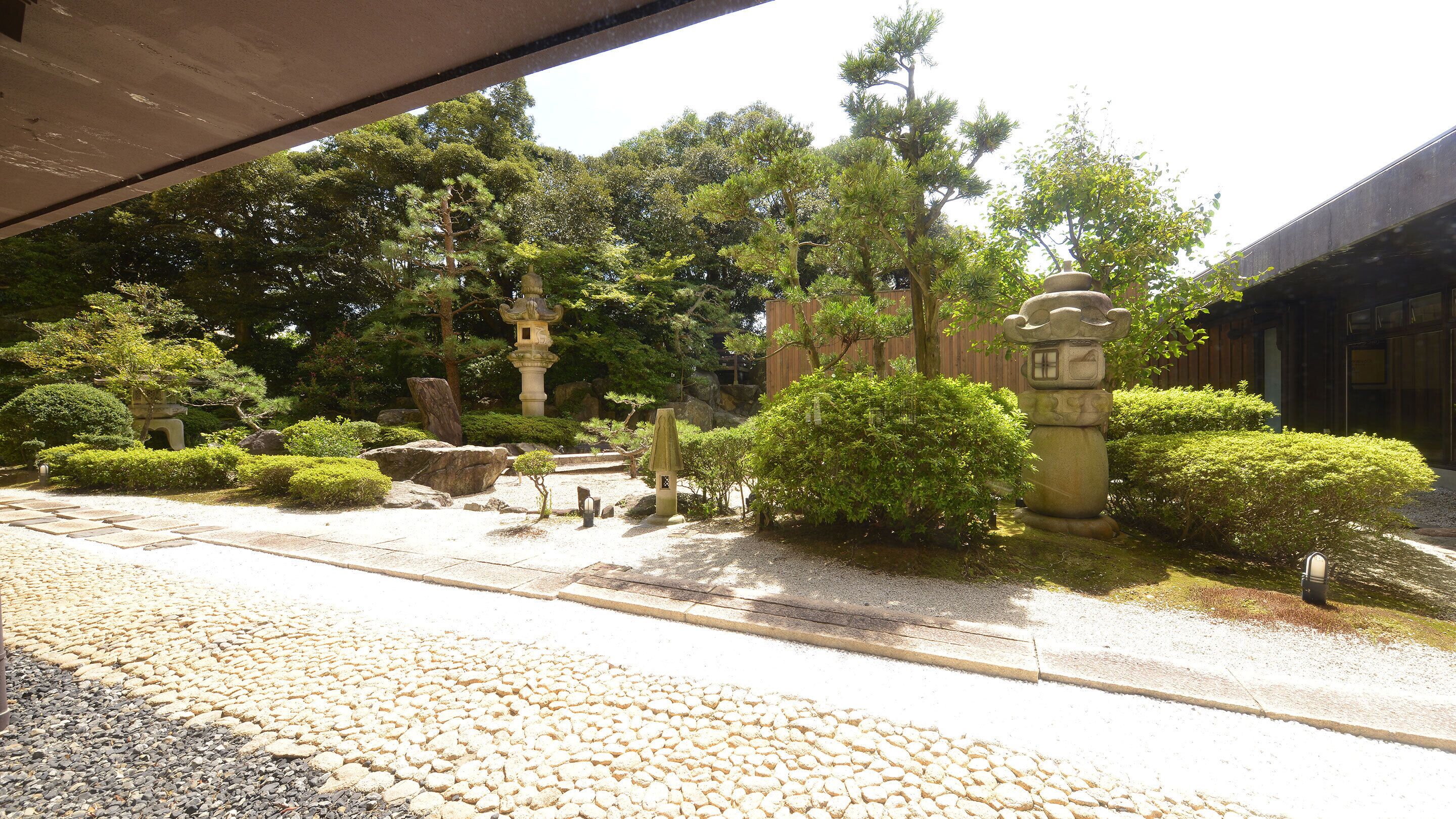 A traditional Japanese garden with stone lanterns, a stone bridge, and neatly trimmed bushes.