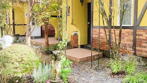 A yellow building with a brick base and a small garden area with a statue and plants. - Gasthof Ami (Nikko)