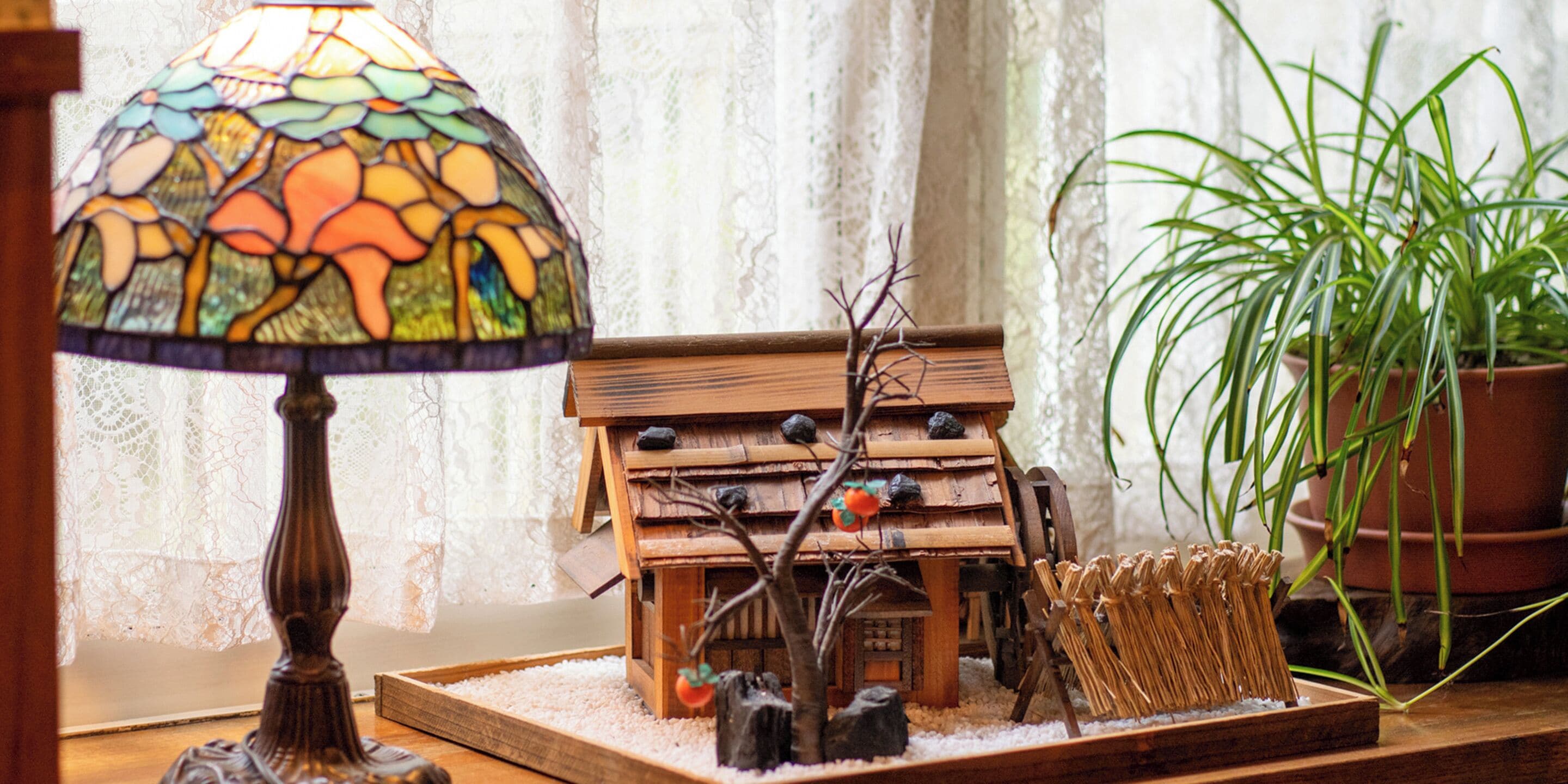 A wooden birdhouse with a small tree and a bird feeder on a windowsill.
