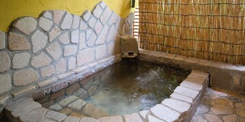 Un manantial de piedra caliente con una valla de bambú y un muro de piedra.