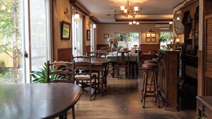 A dining area with wooden tables and chairs, a bar with stools, and a fireplace. - Gasthof Ami (Nikko)