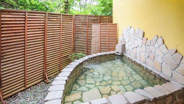 A stone hot tub surrounded by a wooden fence and a yellow wall. - Gasthof Ami (Nikko)