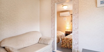 Una camera d'albergo con un divano, un letto con biancheria da letto floreale, un comodino con una lampada e un condizionatore d'aria a parete.
