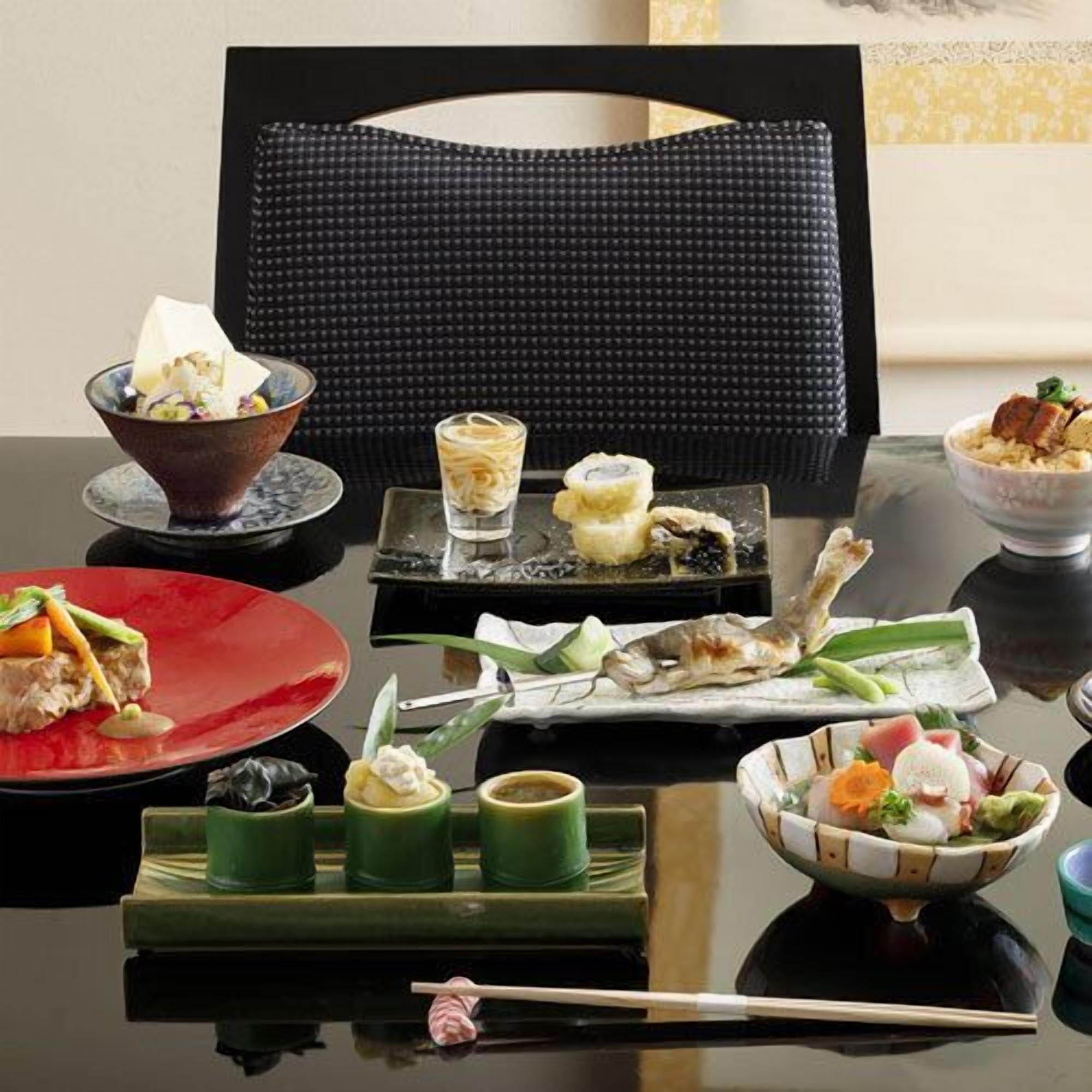 A dining table with various dishes, chopsticks, and a black woven chair.