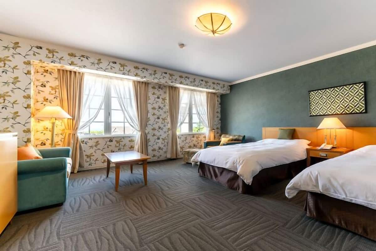 Habitación de hotel con dos camas, un escritorio, una silla, una lámpara y una ventana con cortinas.