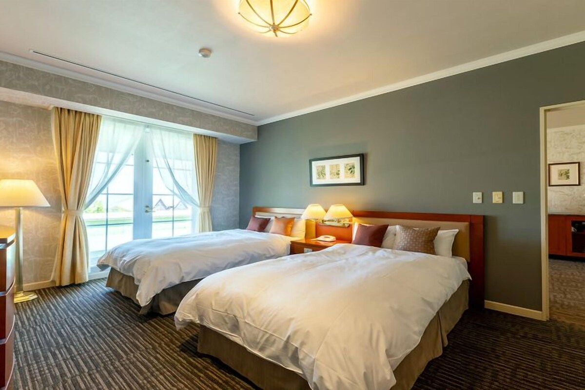 Habitación de hotel con dos camas, un escritorio, una lámpara y vistas a través de la ventana.